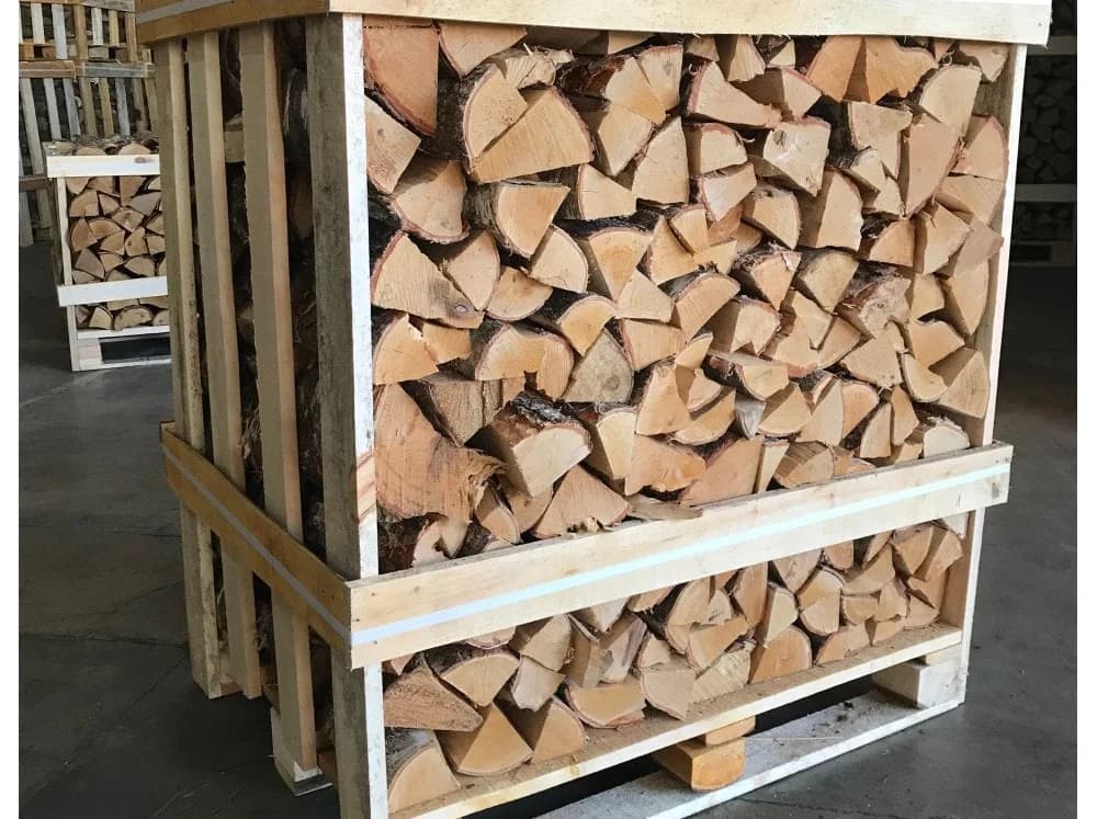 A slatted wooden crate packed with split birch logs, stacked in a timber yard with further crates behind