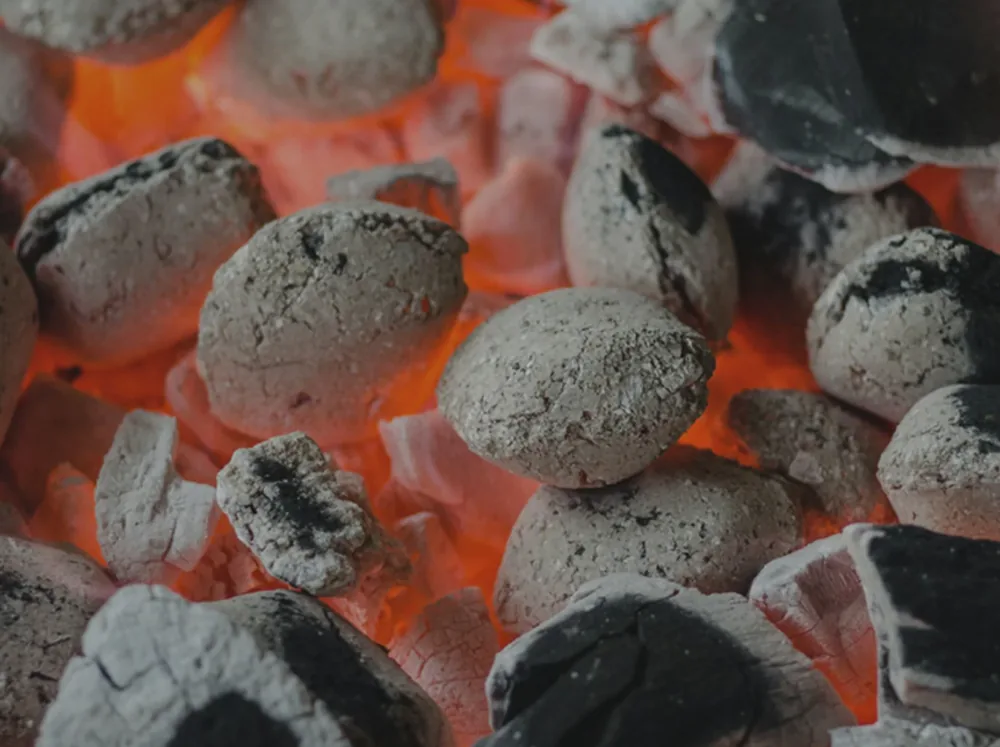 Country Blend solid fuel burning in a grate, ash-greyed briquettes and black coal pieces glowing orange from beneath