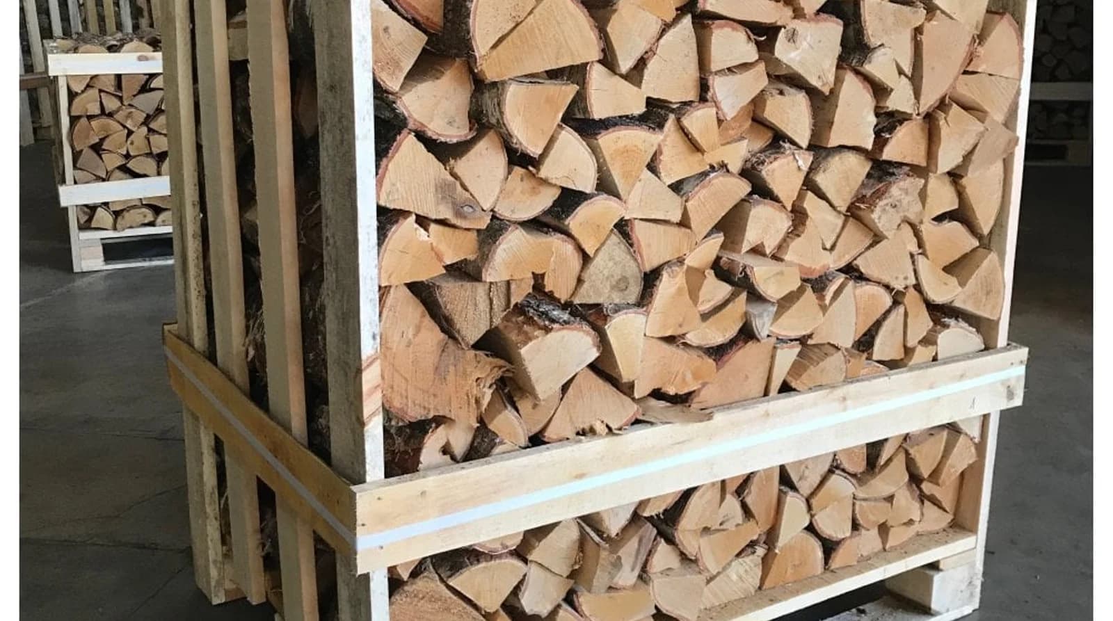 Crates of split logs stacked in a timber yard, pale cut faces packed tight behind the crate slats